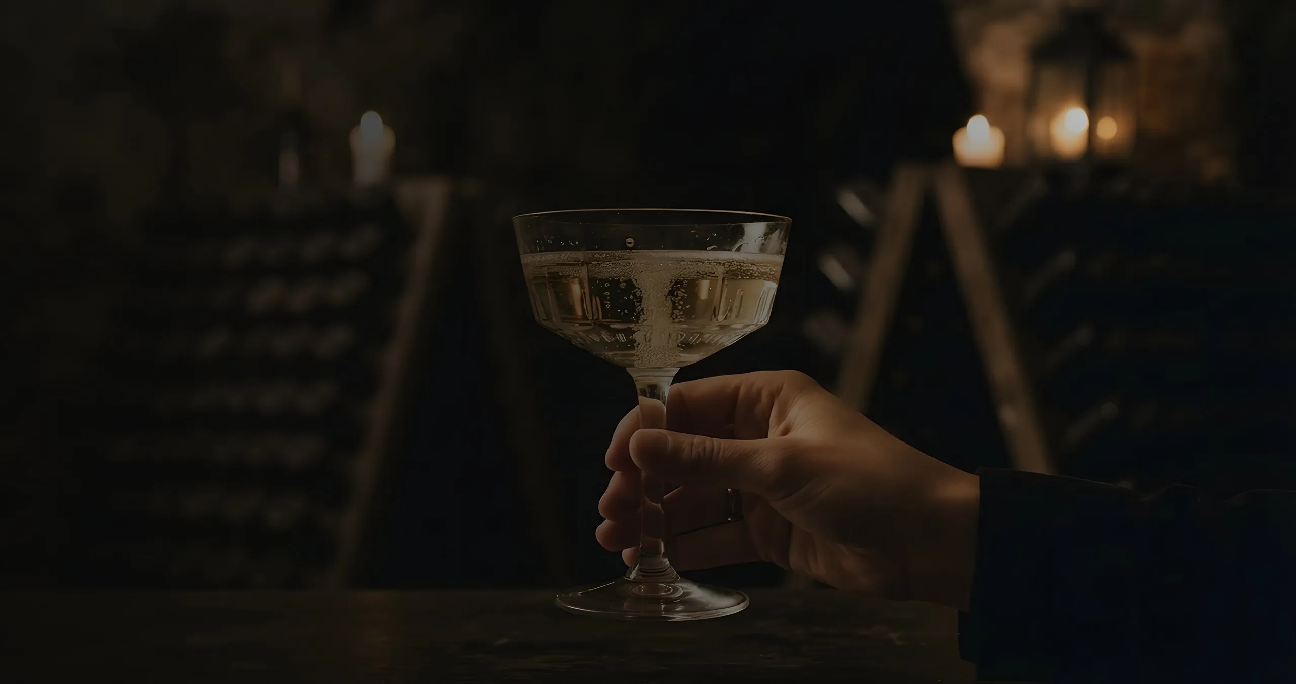 A coupe of champagne held by candlelight, in the cellar
